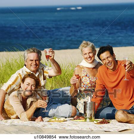 Portrait of two mature couples sitting on the beach and holding champagne flutes View Large Photo Image Picture - Portrait of two mature couples sitting on the beach and holding champagne flutes. Fotosearch
