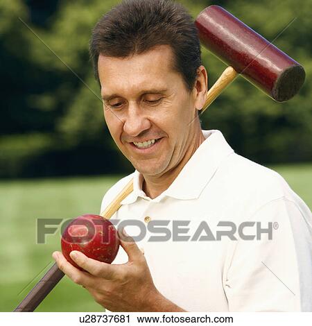 Stock Image - Close-up of a mature man holding a croquet mallet and a ball. Fotosearch