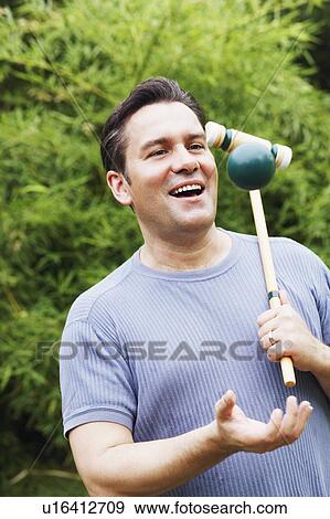 Stock Photo - Close-up of a mature man holding a croquet mallet and tossing a ball. Fotosearch