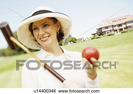 Stock Photograph - Close-up of a mid adult woman holding a croquet mallet and a ball. Fotosearch