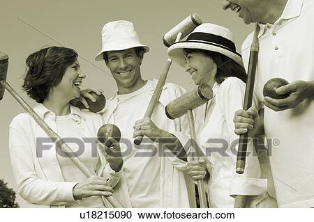 Stock Image - Low angle view of a mid adult couple and a mature couple holding croquet mallets and balls. Fotosearch