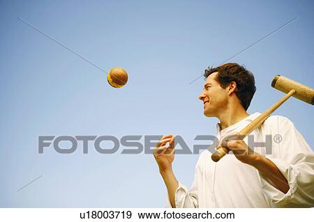 Stock Photo - Low angle view of a mid adult man tossing a ball and holding a croquet mallet. Fotosearch