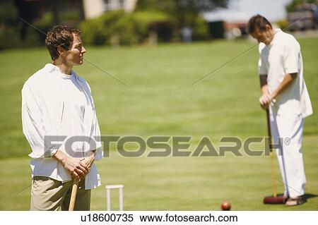 Mid adult man holding a croquet mallet with a mature man standing in the background View Large Photo Image Stock Photography - Mid adult man holding a croquet mallet with a mature man standing in the background. Fotosearch
