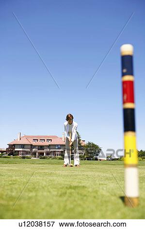 Stock Photo - Mid adult woman playing croquet in a playing field. Fotosearch