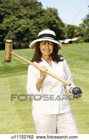 Stock Image - Portrait of a mature woman holding a croquet mallet and a ball. Fotosearch