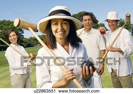 Stock Image - Portrait of a mature woman holding a croquet mallet and a ball with a mid adult couple and a mature man standing behind her. Fotosearch