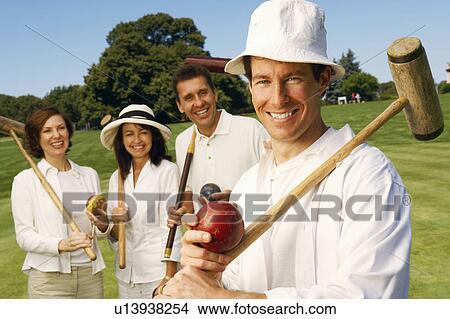 Picture - Portrait of a mid adult man holding a croquet mallet and a ball with a mature couple and a mid adult woman standing behind him. Fotosearch
