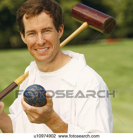Stock Image - Portrait of a mid adult man holding a croquet mallet and a ball. Fotosearch