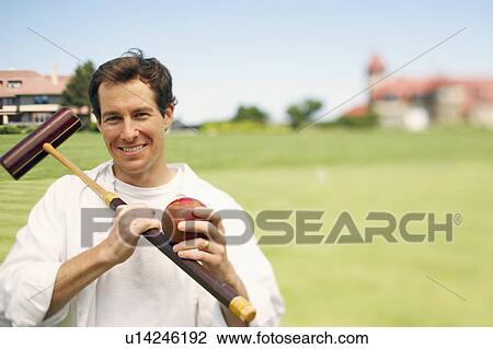 Stock Image - Portrait of a mid adult man holding a croquet mallet and a ball. Fotosearch