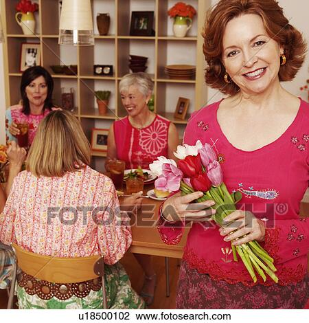 Portrait of a mature woman holding a bouquet of flowers and her friends sitting at the dining table in the background View Large Photo Image Stock Image - Portrait of a mature woman holding a bouquet of flowers and her friends sitting at the dining table in the background. Fotosearch