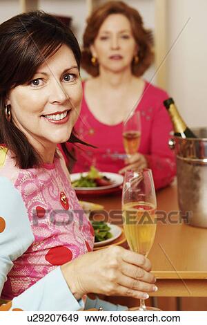Portrait of a mature woman holding a champagne flute with another woman sitting beside her View Large Photo Image Stock Photo - Portrait of a mature woman holding a champagne flute with another woman sitting beside her. Fotosearch