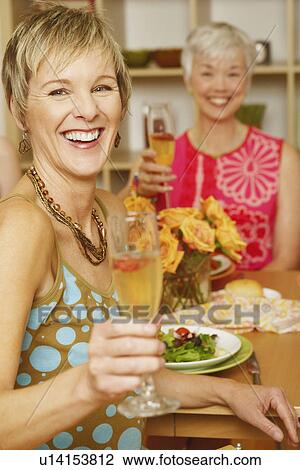 Portrait of a mature woman sitting at the dining table with her friend and holding a champagne flute View Large Photo Image Stock Image - Portrait of a mature woman sitting at the dining table with her friend and holding a champagne flute. Fotosearch