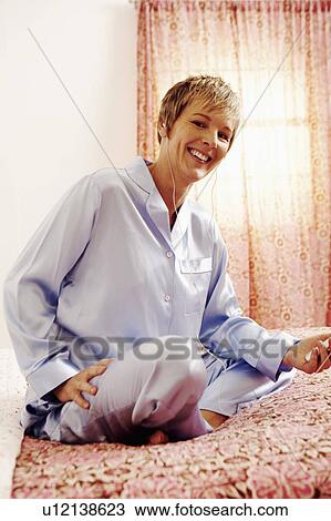 Portrait of a mature woman sitting on the bed and listening to an MP3 player View Large Photo Image Stock Image - Portrait of a mature woman sitting on the bed and listening to an MP3 player. Fotosearch