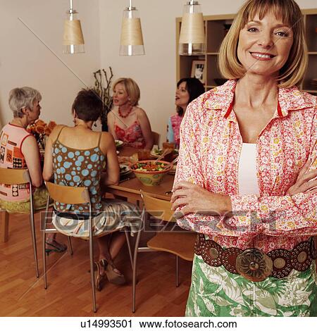 Stock Image - Portrait of a mature woman smiling and her friends sitting at the dining table in the background. Fotosearch