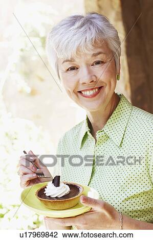 Stock Image - Portrait of a senior woman eating a tart with a fork. Fotosearch