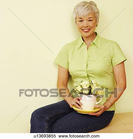 Stock Photography - Portrait of a senior woman holding a coffee cup and smiling. Fotosearch