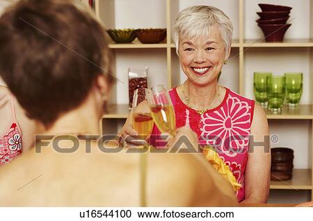 Stock Image - Two women toasting with champagne flutes. Fotosearch