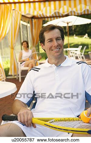 Close-up of a mid adult man sitting on a chair holding a tennis ball and a tennis racket View Large Photo Image Stock Photo - Close-up of a mid adult man sitting on a chair holding a tennis ball and a tennis racket. Fotosearch
