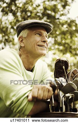 Mature man leaning on a golf bag and smiling View Large Photo Image Stock Image - Mature man leaning on a golf bag and smiling. Fotosearch