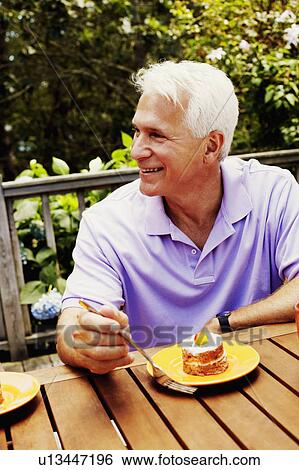 Stock Photograph - Mature man sitting with a plate of dessert in front of him and smiling. Fotosearch