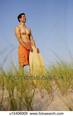Mature man standing on the beach and holding a wooden surfboard View Large Photo Image Stock Photo - Mature man standing on the beach and holding a wooden surfboard. Fotosearch