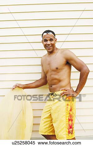 Stock Photography - Portrait of a mature man holding a surfboard and smiling. Fotosearch