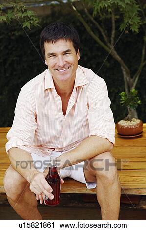 Portrait of a mature man sitting on a table and holding a bottle of red wine View Large Photo Image Stock Image - Portrait of a mature man sitting on a table and holding a bottle of red wine. Fotosearch