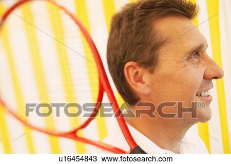 Stock Image - Side profile of a mature man holding a tennis racket and smiling. Fotosearch