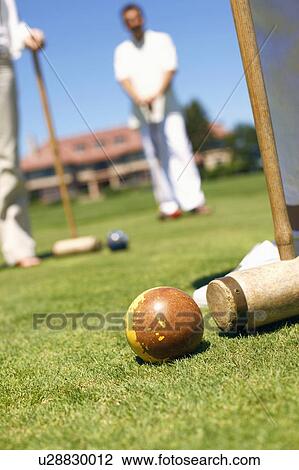 Stock Image - Three people holding croquet mallets in a playing field. Fotosearch