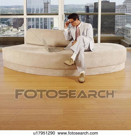 Stock Image - Businessman sitting on a couch and using a laptop. Fotosearch