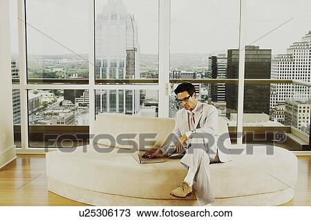 Businessman sitting on a couch and using a laptop View Large Photo Image Stock Image - Businessman sitting on a couch and using a laptop. Fotosearch