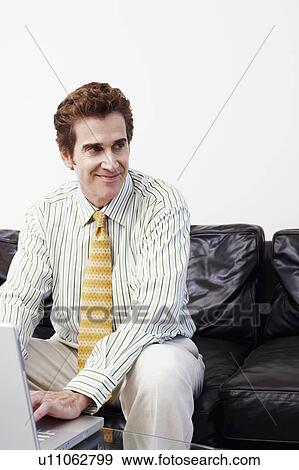 Businessman sitting on a couch and using a laptop View Large Photo Image Stock Photo - Businessman sitting on a couch and using a laptop. Fotosearch