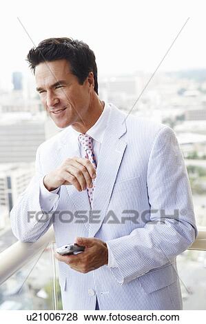 Stock Photo - Close-up of a businessman leaning against a railing and holding a personal data assistant. Fotosearch