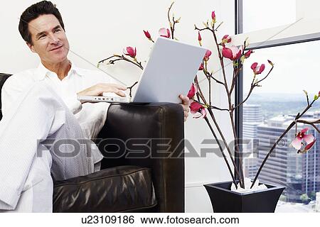 Stock Photograph - Mature man sitting on a couch and using a laptop. Fotosearch