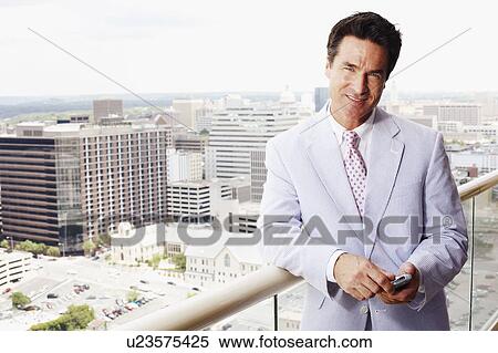 Portrait of a businessman holding a mobile phone and smiling View Large Photo Image Stock Photography - Portrait of a businessman holding a mobile phone and smiling. Fotosearch