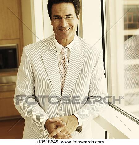 Stock Photo - Portrait of a businessman leaning against a window and smiling. Fotosearch