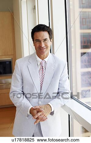 Stock Photography - Portrait of a businessman leaning against a window and smiling. Fotosearch