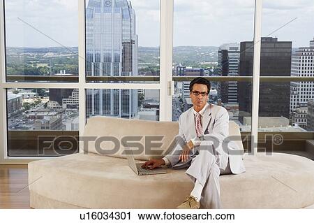 Stock Image - Portrait of a businessman sitting on a couch and using a laptop. Fotosearch