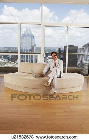Stock Photo - Portrait of a businessman sitting on a couch and using a laptop. Fotosearch