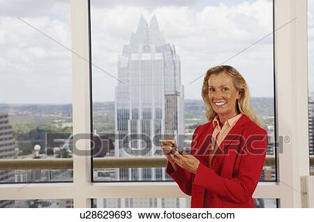 Stock Image - Portrait of a businesswoman using a personal data assistant and smiling. Fotosearch
