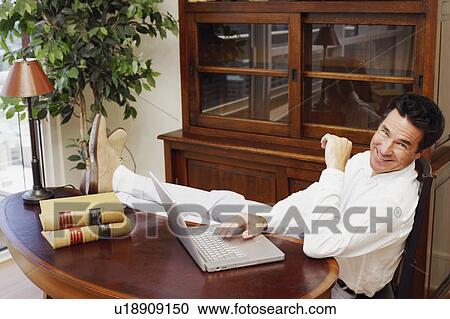 Stock Image - Portrait of a mature man using a laptop and smiling. Fotosearch
