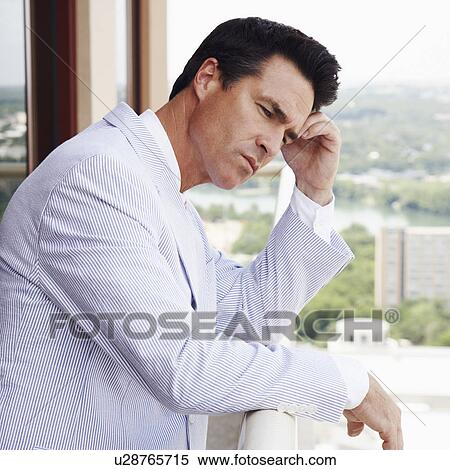 Stock Photography - Side profile of a businessman leaning against a railing and thinking. Fotosearch
