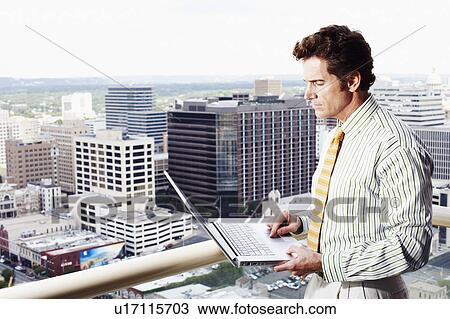 Stock Image - Side profile of a businessman using a laptop in a balcony. Fotosearch