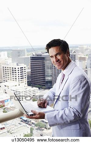 Stock Photography - Side profile of a businessman using a laptop in a balcony. Fotosearch