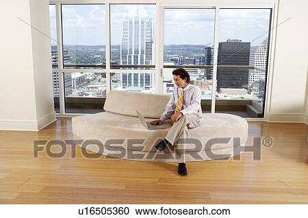 Stock Image - Businessman sitting on a couch and using a laptop. Fotosearch