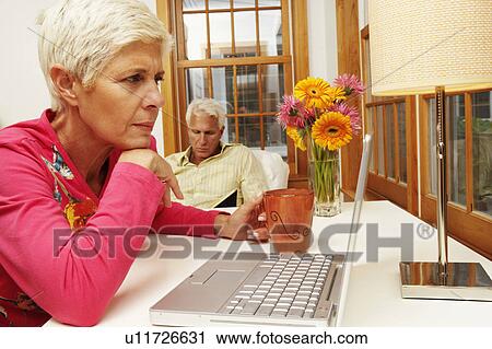 Stock Image - Close-up of a senior woman looking at a laptop with a mature man sitting behind her. Fotosearch