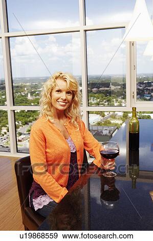 Stock Photo - High angle view of a mid adult woman holding a glass of wine and smiling. Fotosearch