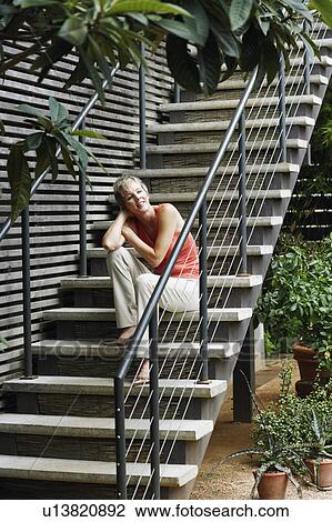 Stock Image - Low angle view of a mature woman sitting on staircase and smiling. Fotosearch