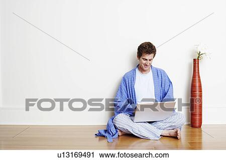 Stock Image - Mature man sitting cross-legged on the floor and using a laptop. Fotosearch