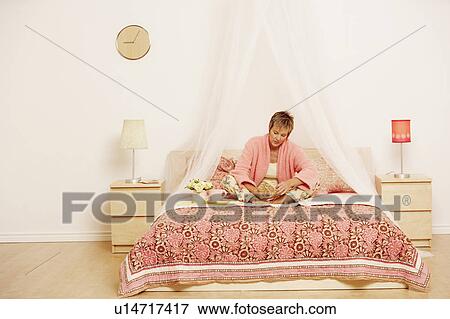 Stock Photo - Mature woman sitting on the bed and reading a book. Fotosearch